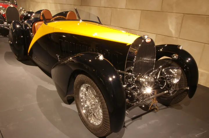 A black and yellow 1934 coachbuilt roadster with long flowing fenders and wire wheels on display in a museum